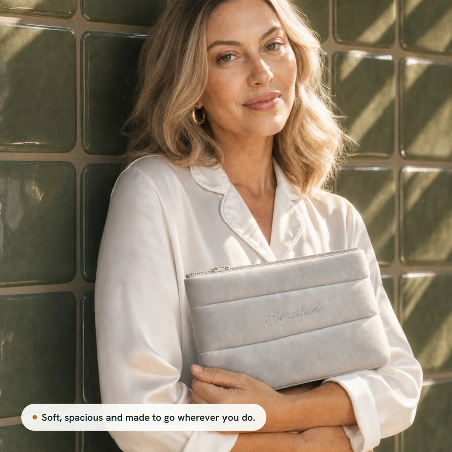 A woman in white silk pyjamas holding the Puffy Beauty Bag